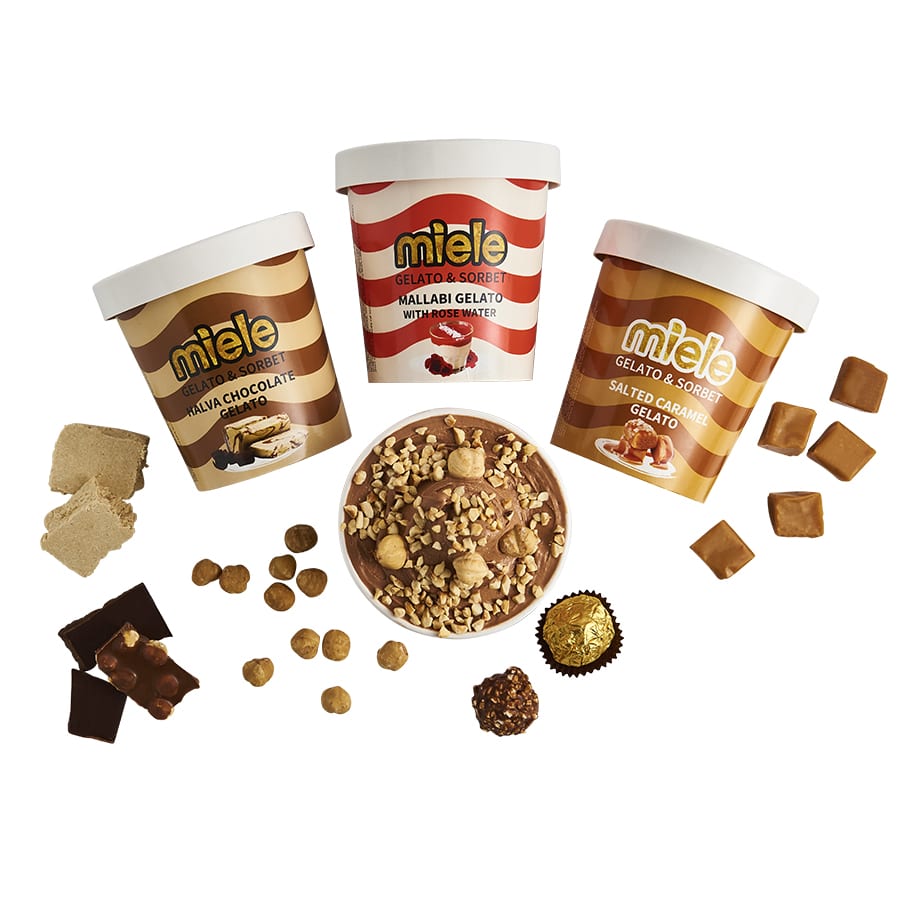 Pints of Salted Caramel Gelato, Halva Chocolate Gelato, Mallabi Gelato, and Roche Gelato surrounded by nuts, chocolate, and caramel pieces