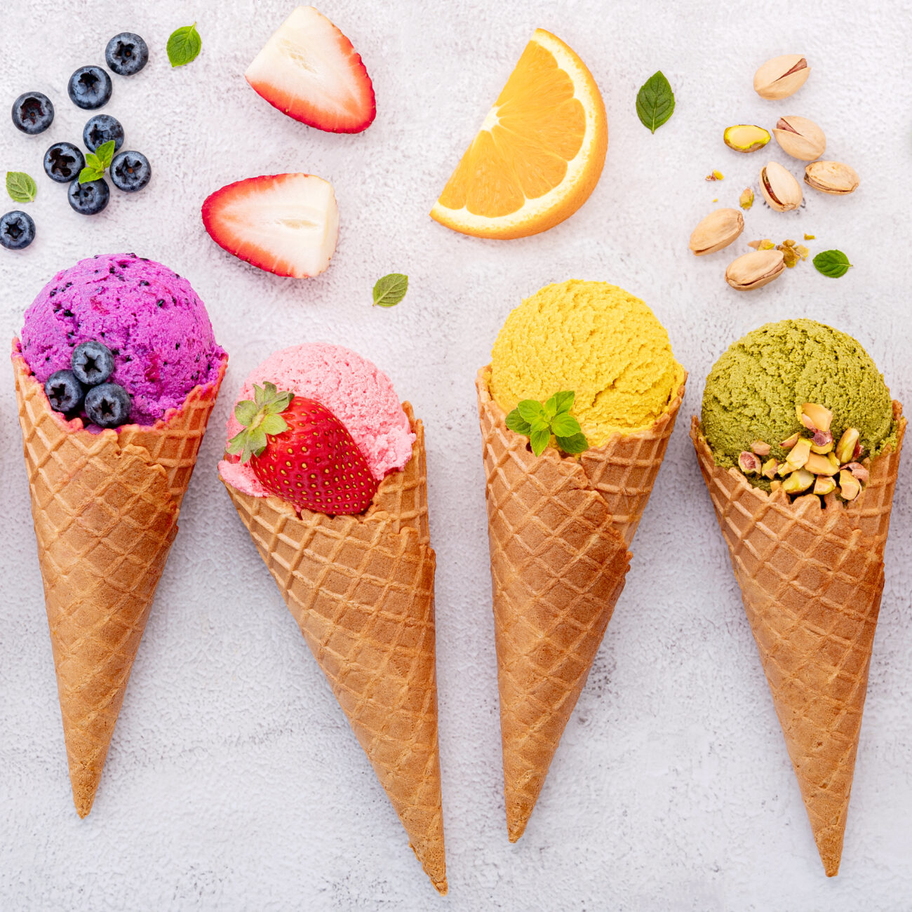 brightly colored gelato in waffle cones with ingredients around the cones
