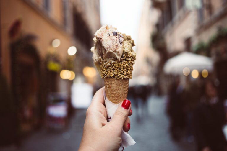 close up of a woman's hand with red nails holding up a cone with gelato